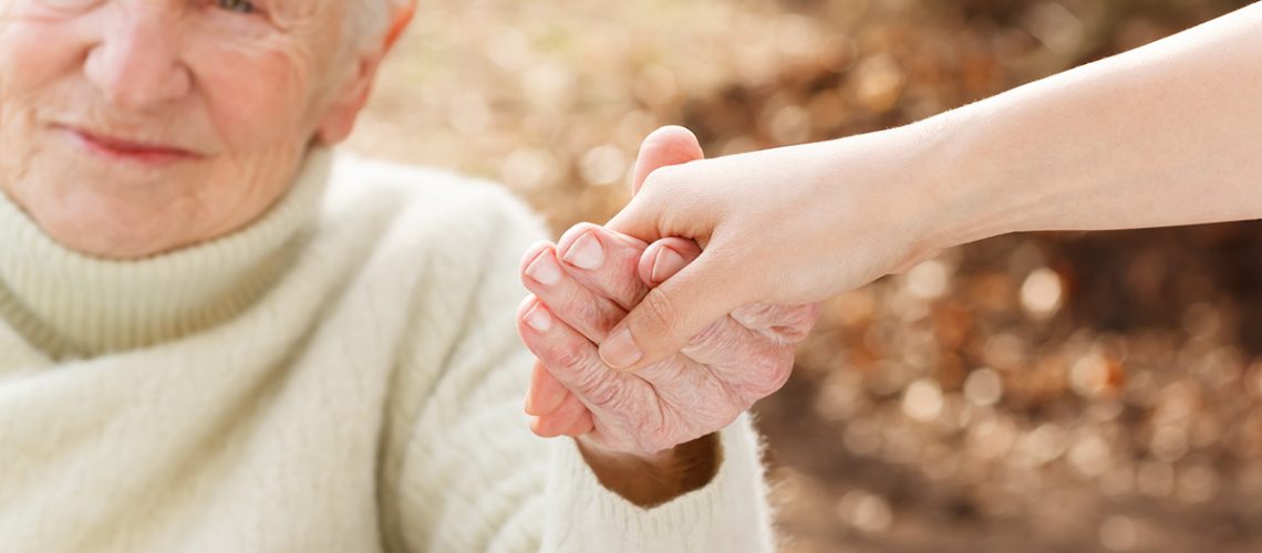 elderly-woman-holding-hands-with-young-woman-outside-SBI-317477652